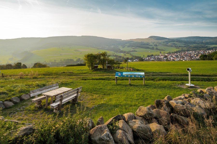 ein Platz mit Fernglas, Sitzganitur und einer Infotafel mit Blick zu den Huten