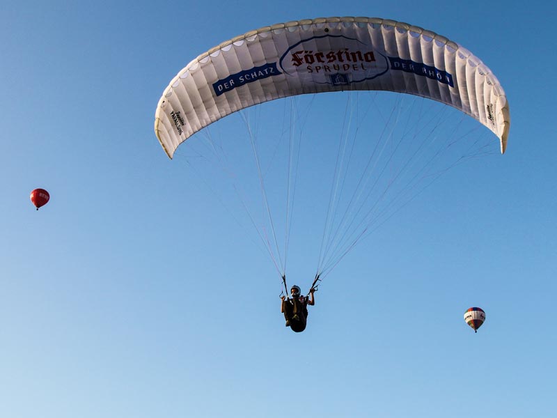 Paraglider und Ballone steigen mit der Strömung in den Himmel hoch hinauf.