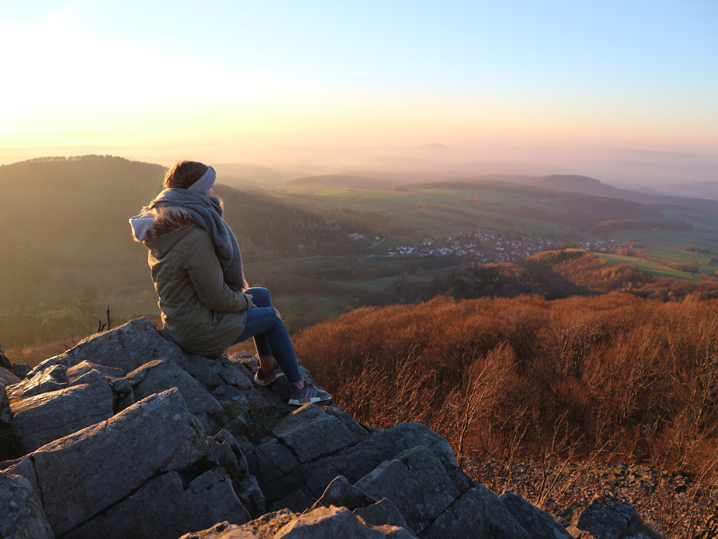 junge Frau sitzt auf den Basaltsteinen auf der Milseburg und genießt die Aussicht